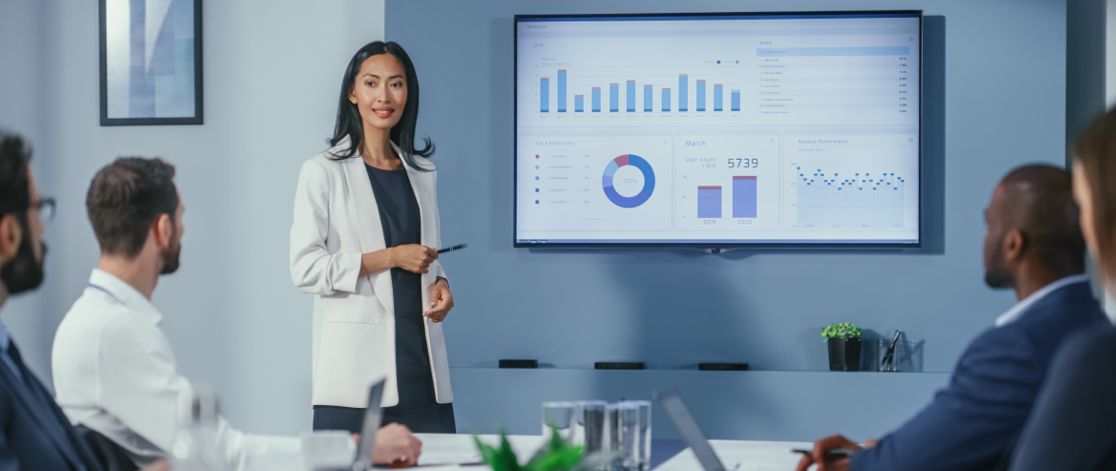 Business woman standing in front of a screen giving a presentation on marketing data in front of her colleagues