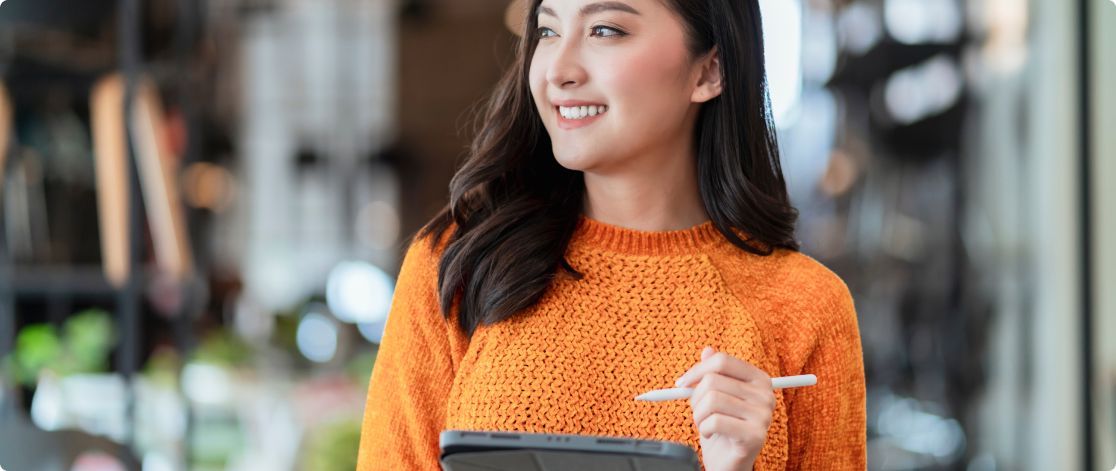 Happy young woman standing in a furniture store taking stock on an iPad 