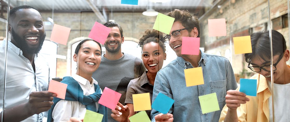 A group of co-workers placing colored sticky notes on a clear board.