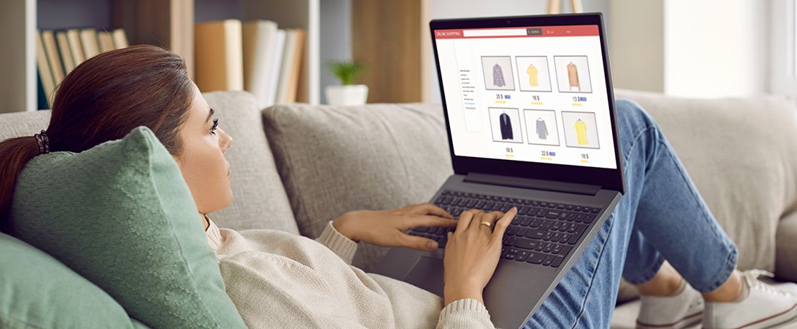 Woman in white sweater laying on the couch browsing clothing eCommerce website