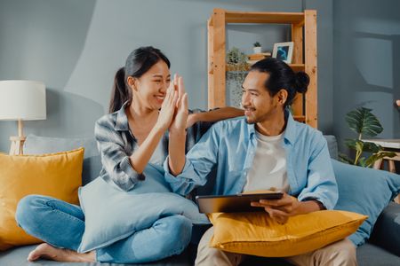 Happy couple high fiving on their couch after buying new furniture on a tablet
