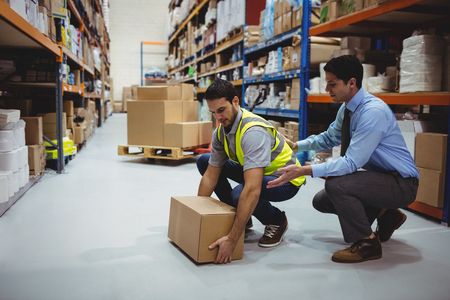 Warehouse manager helping assist new employee to pick up boxes correctly