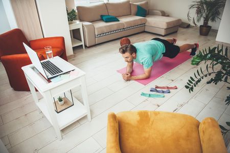 Man doing yoga watching a laptop at home