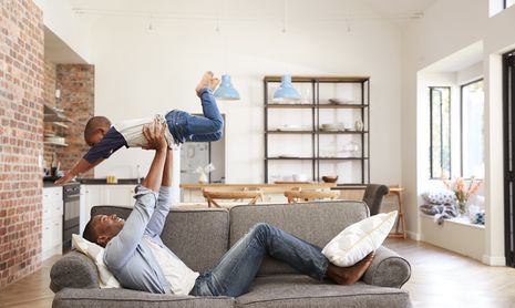 African father and son playing on a couch in a modern new home 